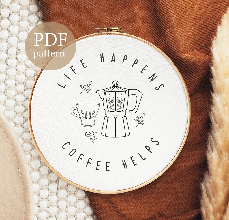 May include: White embroidery hoop with black line art of a coffee pot, coffee cup, and the text "Life Happens Coffee Helps".