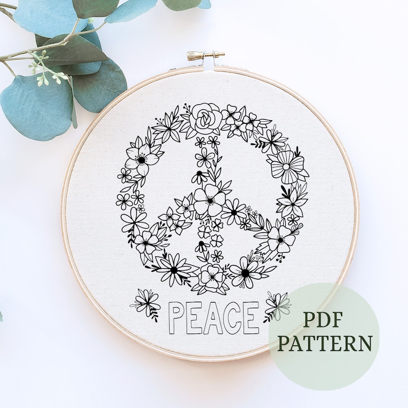 May include: A black and white embroidery pattern of a peace sign surrounded by flowers. The word "PEACE" is written below the peace sign. The pattern is on a white fabric background and is in a round embroidery hoop. The text "PDF PATTERN" is written in a green circle in the lower right corner of the image.