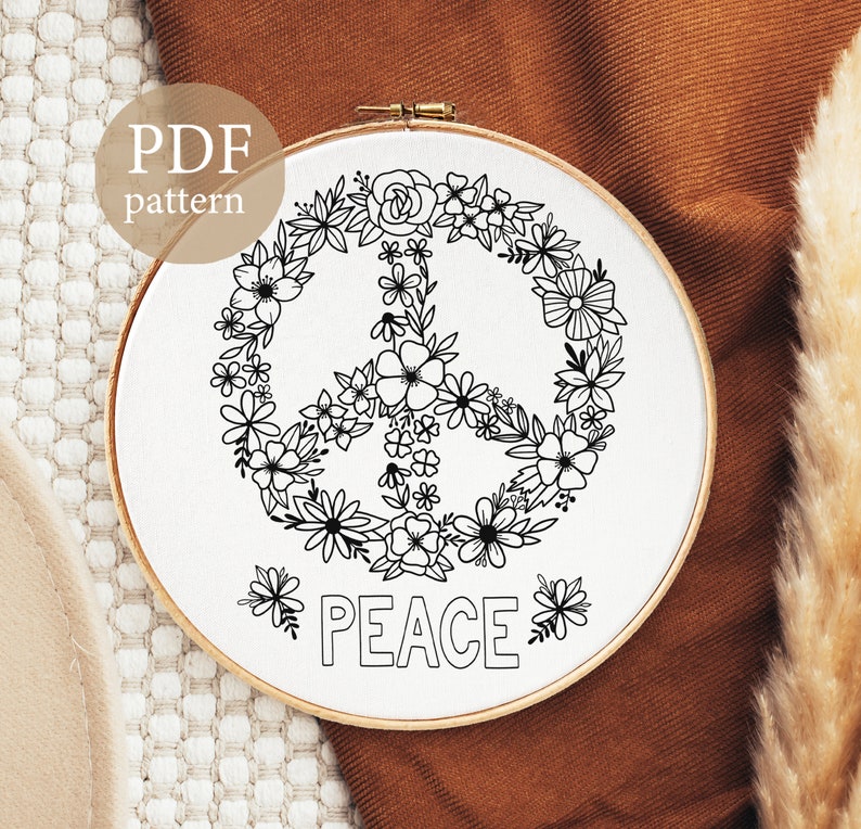 May include: A black and white embroidery pattern of a peace sign surrounded by flowers. The pattern is on a white background and includes the word "PEACE" below the peace sign.