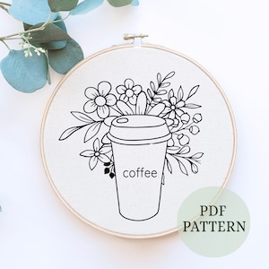 May include: Black and white line art embroidery pattern of a coffee cup with flowers. The pattern is in a hoop and says "coffee" on the cup. The text "PDF PATTERN" is in the lower right corner.