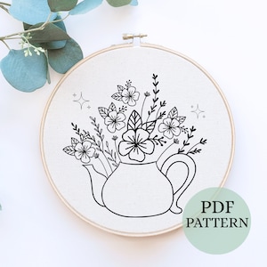 May include: Black and white line art embroidery pattern of a teapot with flowers in it. The pattern is in a hoop and says "PDF PATTERN" at the bottom.