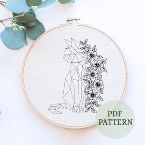May include: A black and white geometric line drawing of a cat with flowers on a white background. The image is in a wooden embroidery hoop. The text "PDF PATTERN" is in a green circle at the bottom of the image.