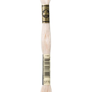 May include: A skein of DMC embroidery floss in color 3770, a light cream color. The floss is wrapped around a cardboard spool with a black and gold label that reads "DMC 25" and "8 m (8.7 yd)".