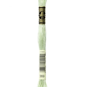 May include: A skein of DMC embroidery floss in color 369, a light green shade. The floss is wound around a white card with black text that reads "DMC" and "25m (8.7 yd)".