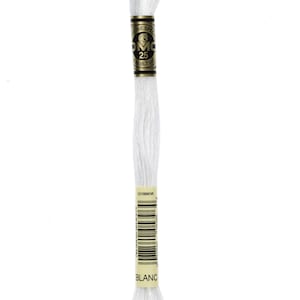 Puede incluir: Un ovillo de hilo de bordar blanco, etiquetado como "Blanc". El hilo está enrollado alrededor de una bobina de cartón con una etiqueta negra y dorada. La etiqueta indica que el hilo es de la marca DMC, tamaño 25, y contiene 8 metros.