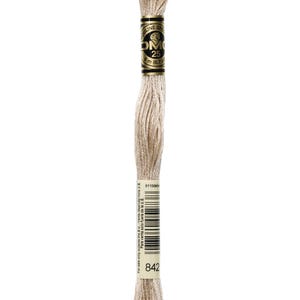 May include: A spool of DMC brand embroidery floss in a light beige color. The label reads "DMC 25" and "8 m (8.7 yds)". The color number "842" is visible. The floss is tightly wound and ready for use in various needlework projects.