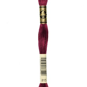 May include: A spool of DMC embroidery floss in color 815, a deep burgundy red. The floss is wound around a white card with the DMC logo and the number 25, indicating the length of the floss. The card also has a barcode and the number 815 printed on it.