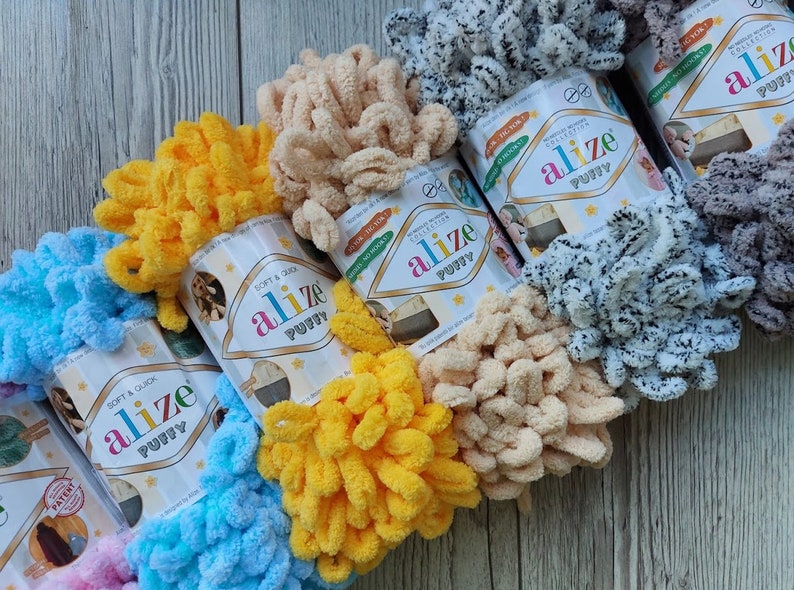 May include: A variety of colorful yarn skeins in different shades of blue, yellow, pink, beige, and gray. The yarn is fluffy and textured, and the skeins are labeled "alize puffy".