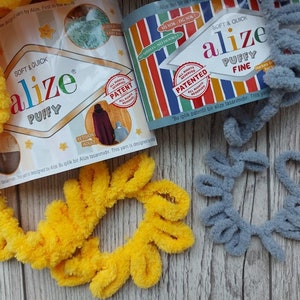 May include: Two skeins of yarn, one yellow and one gray, with the Alize brand label visible. The label says "Soft & Quick" and "Puffy" for the yellow yarn and "Soft & Quick" and "Puffy Fine" for the gray yarn.