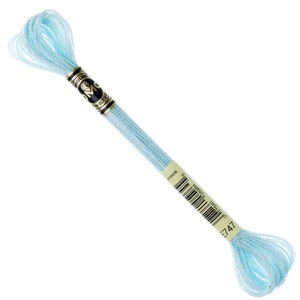 May include: A skein of light blue embroidery floss. The floss is wrapped around a black and gold label with the brand name. The color code E747 is visible on the label. The floss is a soft, pastel blue color.