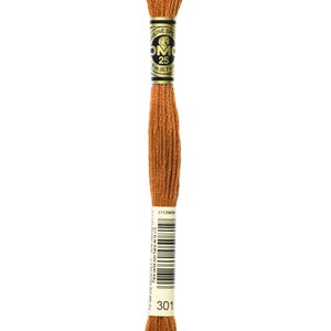 May include: A spool of DMC embroidery floss in color 301, a brown shade. The spool is labeled with the DMC logo and the number 25, indicating the length of the floss.