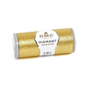Puede incluir: Un carrete de hilo DMC Diamant Grandé dorado claro. El hilo está enrollado alrededor de un carrete gris con una etiqueta blanca que dice "DIAMANT GRANDÉ". El texto "G3821- light gold" está debajo.