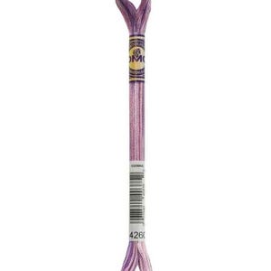 May include: A skein of DMC embroidery floss in shades of lavender and light purple. The floss is wrapped with a paper label that includes the number 4260 and a barcode. The top and bottom of the floss are looped.