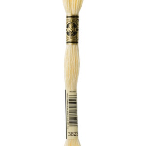 Pode incluir: Um novelo de fio para bordar DMC na cor 3823, um amarelo claro. O fio está enrolado em torno de um carretel de cartão com um rótulo dourado que diz "DMC Special 25 8.7 yd".