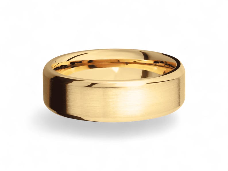 Op de afbeelding: Een goudkleurige ring met een geborstelde afwerking. De ring heeft een platte, brede band en een afgeronde binnenkant. De ring is waarschijnlijk gemaakt van goud en is ontworpen voor dagelijks gebruik.