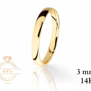 Può includere: Un anello in oro lucido, largo 3 mm, con timbro 14K. L'anello è posto su uno sfondo bianco, con un riflesso visibile sotto. Il logo KVS Jewelry si trova nell'angolo in basso a sinistra.