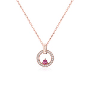 May include: A rose gold necklace with a small circle pendant featuring a pink gemstone and a row of clear cubic zirconia stones. The pendant has a small rectangular tag hanging from it that says "LOVE".