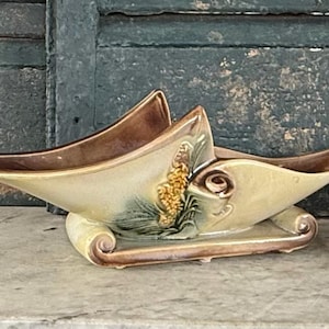 May include: A vintage ceramic centerpiece bowl in a boat shape. The bowl features a cream-colored base with brown accents and a decorative floral design. The bowl is approximately 12 inches long.