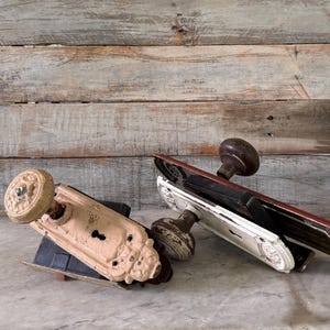May include: An assortment of antique door hardware, including doorknobs and backplates. The hardware features a variety of colors, including cream, brown, and white. The items are arranged on a marble surface against a wooden background.