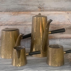 May include: A collection of vintage brass coffee and tea serving pieces. The set includes a tall coffee pot, a creamer, a sugar bowl, and a small serving pot. Each piece has a black handle.