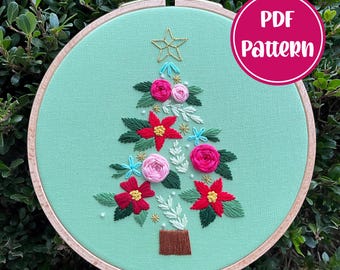 Peut inclure: Un modèle PDF pour un projet de broderie d'arbre de Noël floral. Le motif représente un arbre vert avec des fleurs roses, rouges et bleues, des feuilles et une étoile dorée au sommet. Le motif est présenté dans un cerceau de broderie en bois.