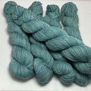 May include: Four skeins of teal blue yarn, arranged in a pile.