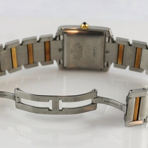 May include: Back view of a Cartier Tank watch with two-tone stainless steel and 18k yellow gold bracelet. The watch features a rectangular case and a deployant clasp.  The watch face is not visible.  'SWISS MADE' and 'STAINLESS STEEL' are visible on the clasp. The Cartier logo is visible on the watch case back.