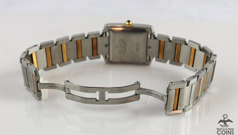May include: Back view of a Cartier Tank watch with two-tone stainless steel and 18k yellow gold bracelet. The watch features a rectangular case and a deployant clasp.  The watch face is not visible.  'SWISS MADE' and 'STAINLESS STEEL' are visible on the clasp. The Cartier logo is visible on the watch case back.