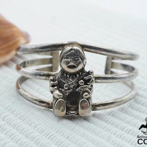 May include: Silver ring with a three-dimensional design of a smiling person holding a flower. The ring has three bands.