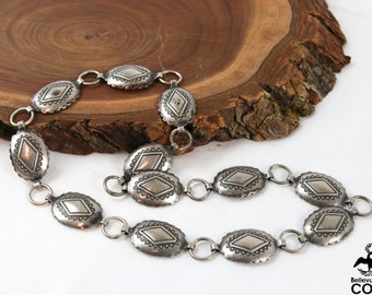 May include: A silver chain belt with oval-shaped links featuring a diamond pattern. The chain is on a wooden surface.