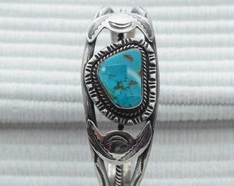 May include: A silver bracelet with a turquoise stone set in a silver bezel. The bracelet has a decorative design with a rope-like pattern and a crescent moon shape on each side of the stone.