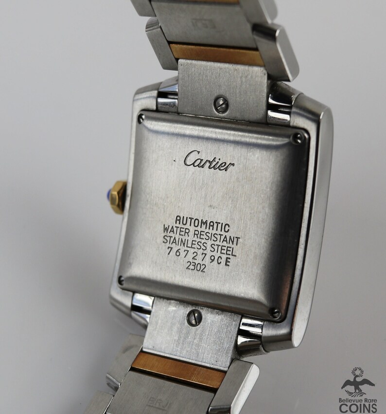 May include: Close-up of the back of a Cartier watch. The stainless steel case back is engraved with 'Cartier', 'Automatic', 'Water Resistant', 'Stainless Steel', '767279CE', and '2302'. The watch features a two-tone band with stainless steel and gold accents. The watch is a classic design with a square face and a polished finish.