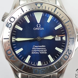 May include: A silver Omega Seamaster Professional Chronometer watch with a blue dial and a date window at the 3 o'clock position. The watch has a stainless steel case and bracelet, and a unidirectional rotating bezel.