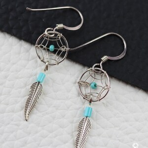Puede incluir: Pendientes de plata con forma de atrapasueños con cuentas turquesas y abalorios de plumas.