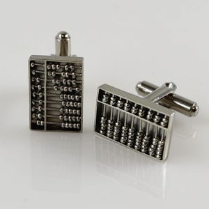 Peut inclure: Une paire de boutons de manchette en argent avec un design d'abaque détaillé. Les boutons de manchette sont en métal et ont une finition polie.