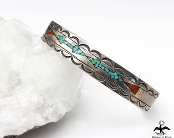 May include: A silver bracelet with turquoise and red stone inlay. The bracelet has a scalloped edge and a repeating pattern of arrowheads.