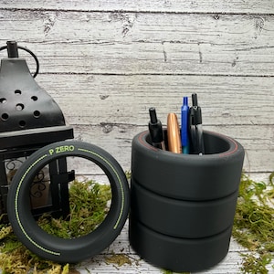 May include: Black tire-shaped desk organizer with a red top rim and a green stripe around the base. The organizer is filled with pens and pencils.