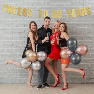 May include: Four friends celebrating a 40th birthday with gold glitter banners, champagne flutes, and metallic balloons. The banner reads "Cheers to 40 Years".
