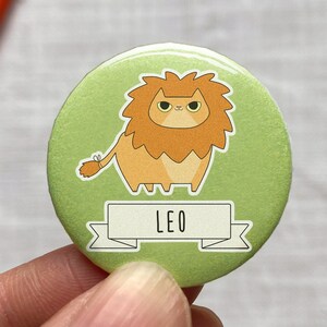 以下が含まれることがあります： たてがみのあるライオンの漫画と「LEO」という文字が書かれたバナーが付いた緑色のボタンです。