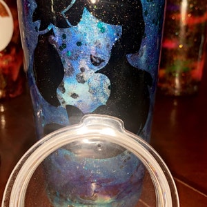 Puede incluir: Un vaso de tem&aacute;tica galaxia azul y morado con una silueta negra de la cara de una mujer. El vaso tiene una tapa transparente.