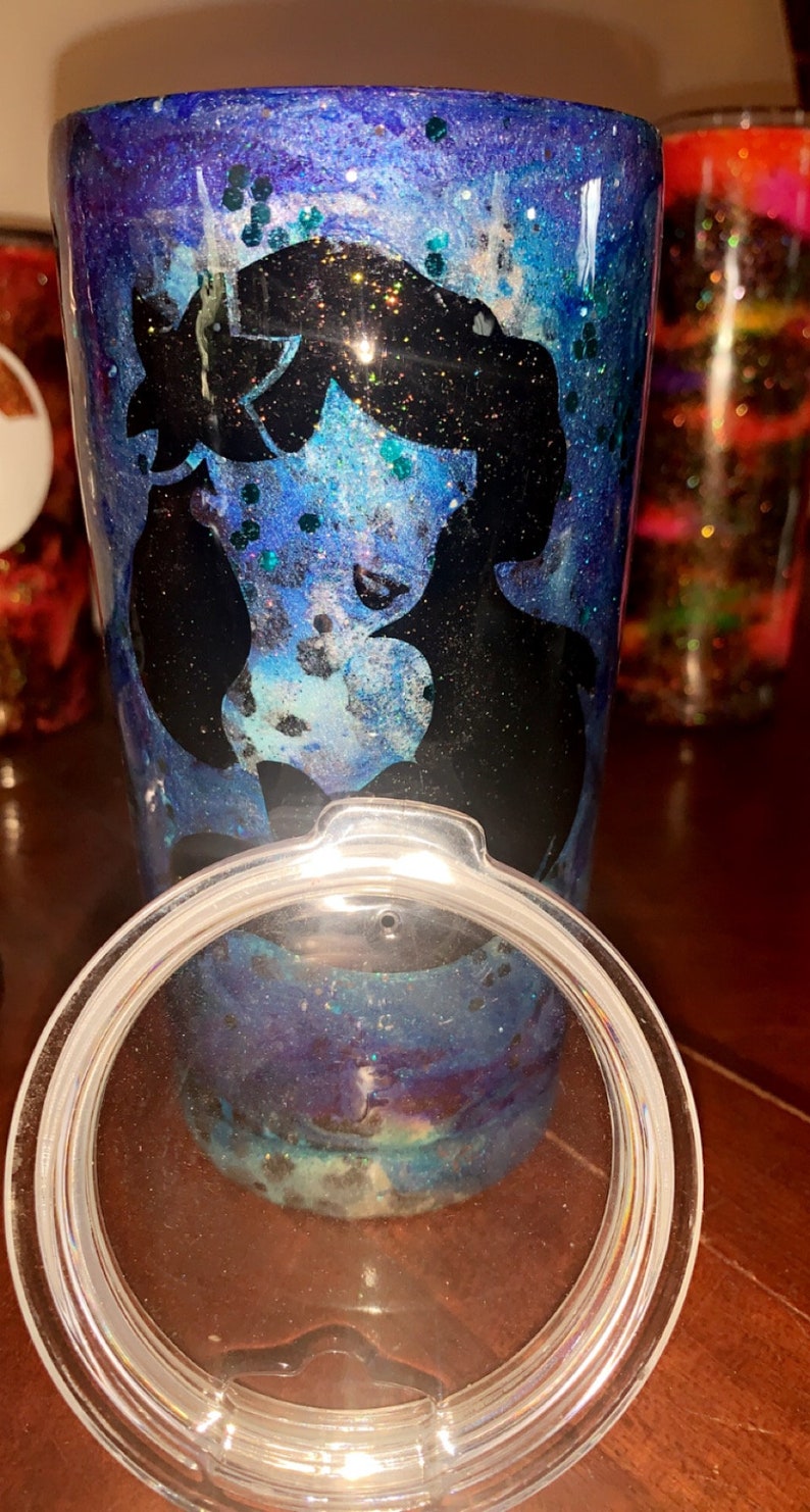 Puede incluir: Un vaso de tem&aacute;tica galaxia azul y morado con una silueta negra de la cara de una mujer. El vaso tiene una tapa transparente.
