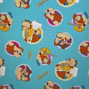 May include: A light blue fabric featuring a repeating pattern of the Disney character Hercules in various action poses. Each character is framed in a yellow circle with the words "HERO" and "HERCULES" in white text. The cartoon Hercules is depicted with brown hair and skin, wearing a red tunic.