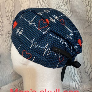 May include: Blue and black skull cap with a white EKG pattern and red hearts. The cap has black ties.