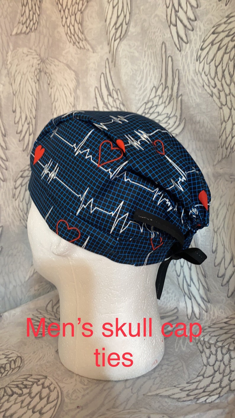 May include: Blue and black skull cap with a white EKG pattern and red hearts. The cap has black ties.