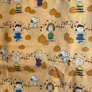 Peut inclure: Tissu à motif répété avec des personnages de dessins animés, des citrouilles et des feuilles d'automne sur un fond jaune clair. Les personnages incluent un chien, un garçon en chemise jaune, une fille en robe bleue et d'autres enfants. Les citrouilles sont oranges.
