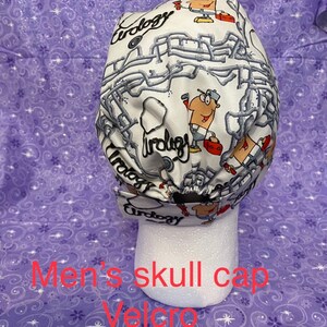 May include: White skull cap with a plumbing themed design. The cap features a cartoon plumber and the word "Urology" repeated throughout the design. The cap has a velcro closure.