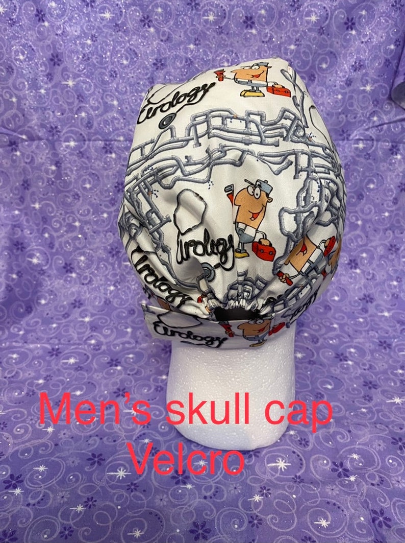 May include: White skull cap with a plumbing themed design. The cap features a cartoon plumber and the word "Urology" repeated throughout the design. The cap has a velcro closure.