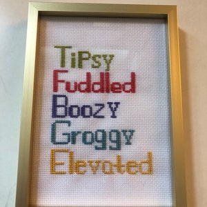May include: A framed cross-stitch with the words "Tipsy", "Fuddled", "Boozy", "Groggy", and "Elevated" in different colors.