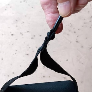 May include: Black exercise resistance band handle with a black foam grip. The handle is attached to a black strap and a black metal rod. The handle is held by a person.