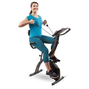 May include: A stationary exercise bike with a black frame and a digital display. The bike has a seat and handlebars, and the person is using resistance bands. The person is wearing a blue top and leggings and black sneakers.